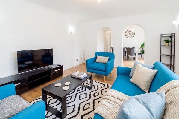 Een moderne woonkamer met een televisie, een blauwe bank en een kamerkleed met patroon.