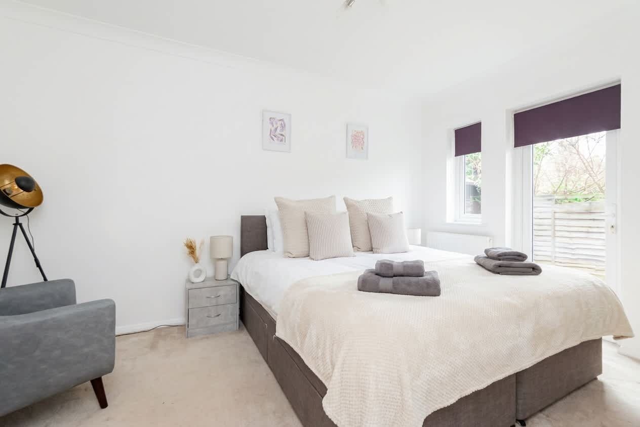 A bedroom with a bed, bedside table, lamp, and a chair.