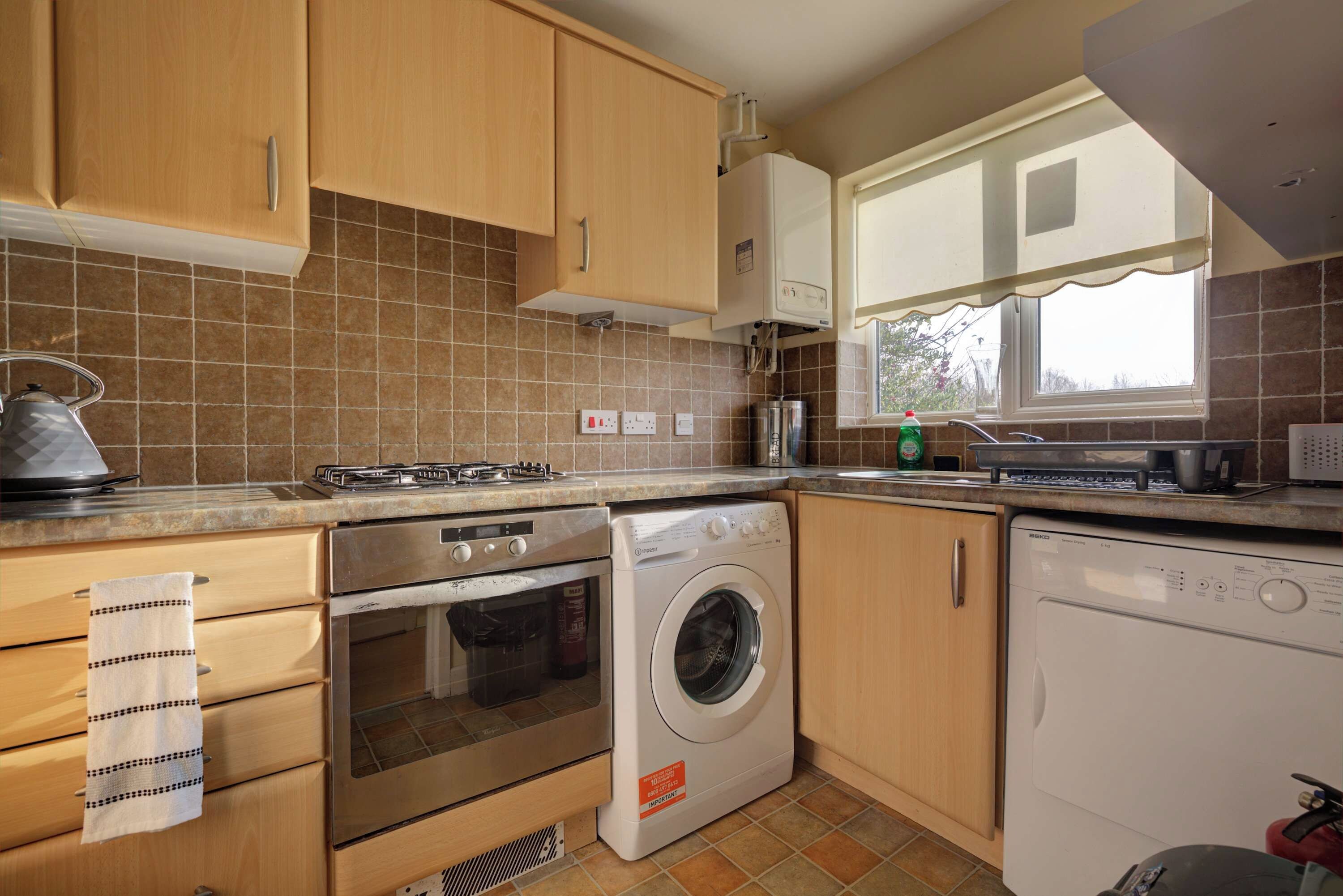 A kitchen with wooden cabinets, a stove, an oven, a washing machine, and a dishwasher.