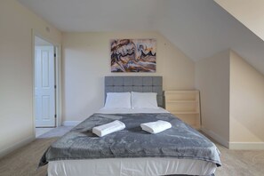 Een slaapkamer met een bed, hoofdbord, schilderij en een deur.