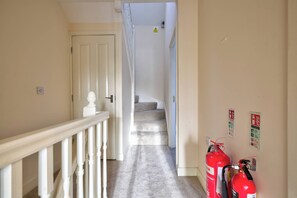 Ein Flur mit weißer Geländer, einem Teppich und zwei an der Wand befestigten Feuerlöschern.