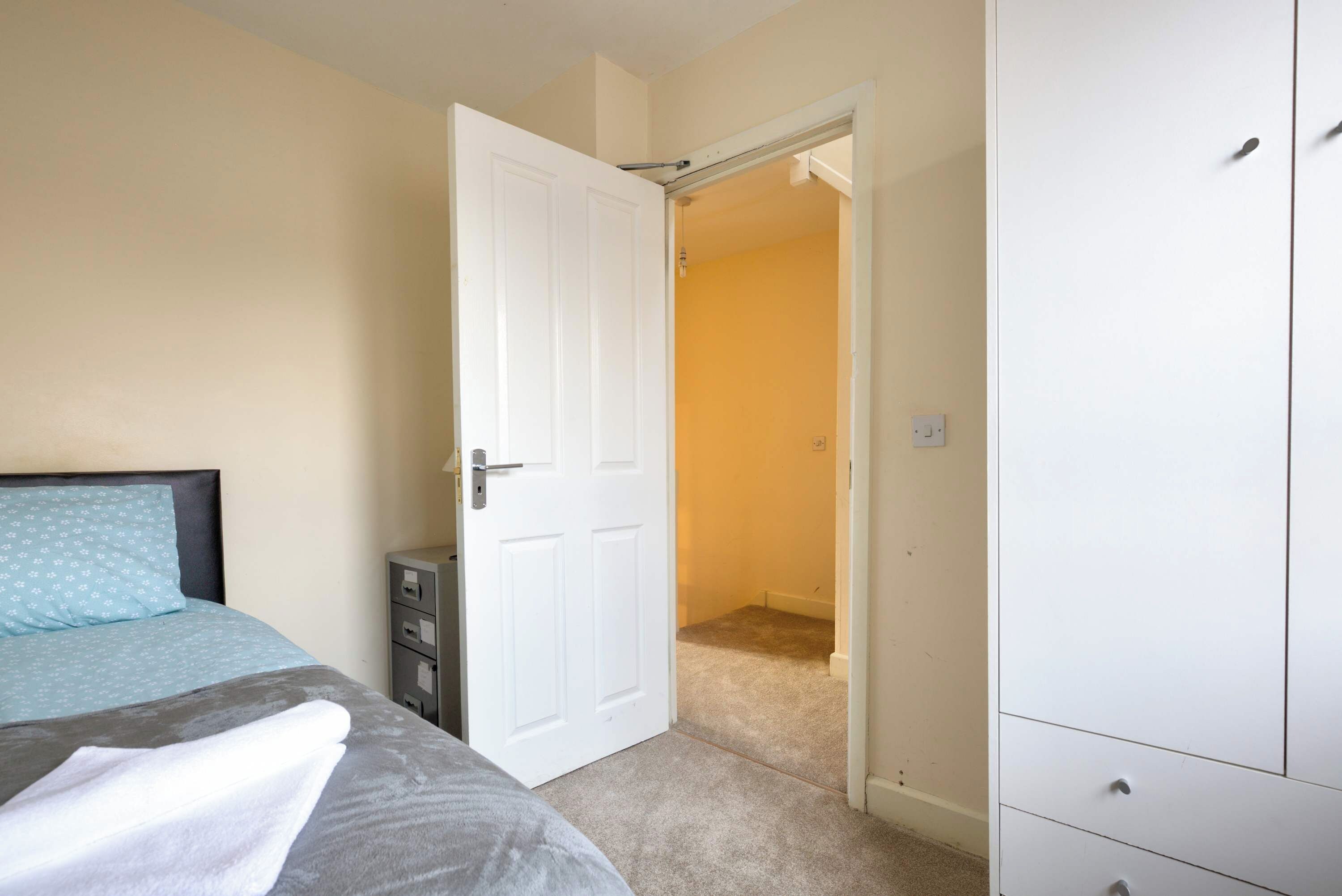 A bedroom with a bed, a wardrobe, and a door leading to another room.