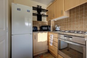Een compacte keuken met een witte koelkast, een magnetron, een gasfornuis en een vaatwasser.