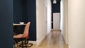 Un pasillo estrecho con suelo de madera, una puerta blanca al final y una mesa con sillas a la izquierda.