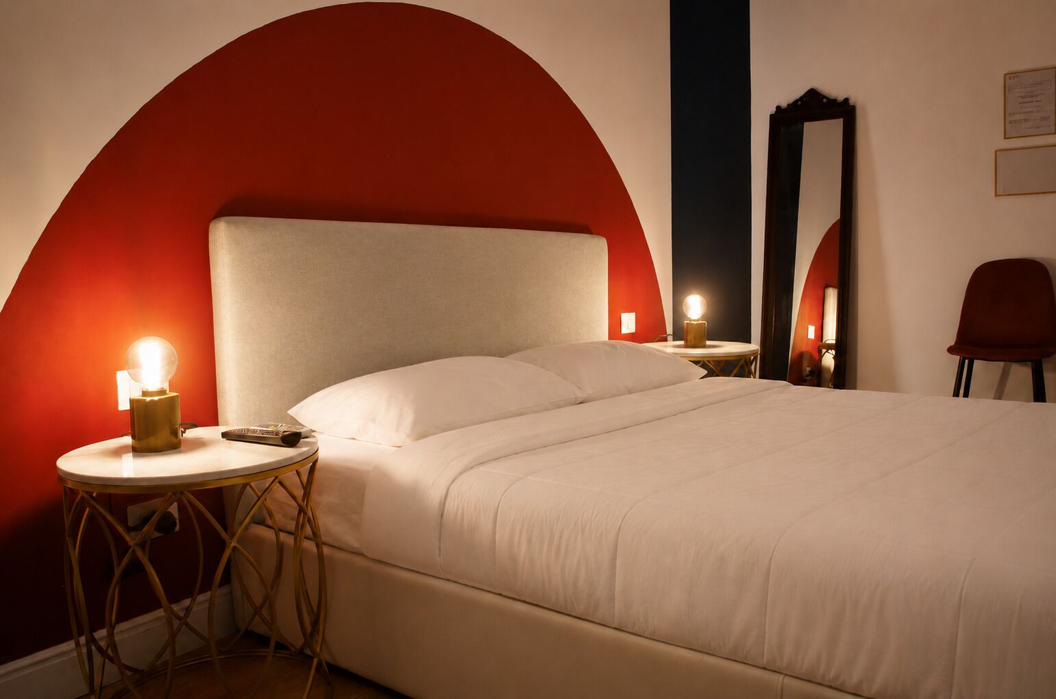 A bed with a headboard, bedside tables, a mirror, and a chair in a room with red and white walls.