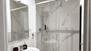 Un baño moderno con cabina de ducha de vidrio, un lavabo blanco y un salpicadero de mármol.