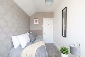 A bedroom with a bed, a bedside lamp, a potted plant, and a framed picture on the wall. - Modern 3BR Home with Free Parking & Fast Wi-Fi (Rugby)