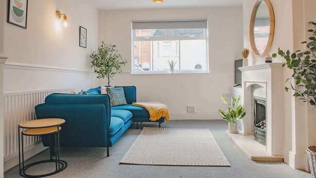 Ein Wohnzimmer mit einem blauen Sofa, einem kleinen runden Tisch, einem Kamin und einem großen Fenster.