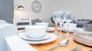 Une table à manger dressée avec des bols, des assiettes, des verres et des couverts blancs, et une horloge et une lampe accrochées au mur.