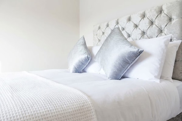 Una cama con cabecera acolchada, ropa de cama blanca y dos almohadas.