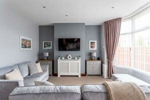 Ein modernes Wohnzimmer mit einem grauen Sofa, einer weißen Unterhaltungseinheit und einem großen Fenster mit Vorhängen.