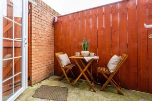 A patio with a wooden table and two chairs, a brick wall, and a wooden fence.