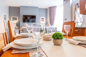 A dining table set with plates, glasses, and a small potted plant, with a modern interior and a television in the background.