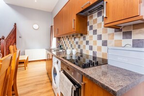 A modern kitchen with wooden cabinets, a tiled backsplash, a built-in oven, and a countertop with a bread rack.