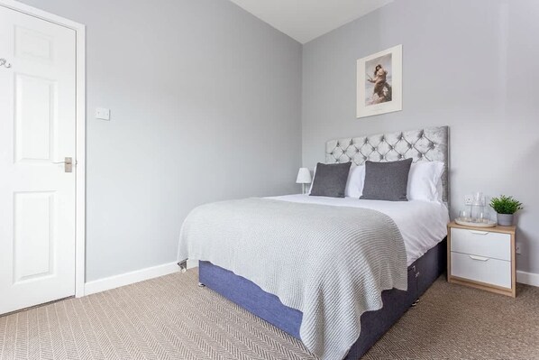 A bedroom with a bed, bedside table, and a wall-mounted picture.