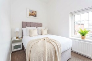 Une chambre d’hôtel avec un lit, une table de chevet, une lampe et une fenêtre donnant sur des immeubles.