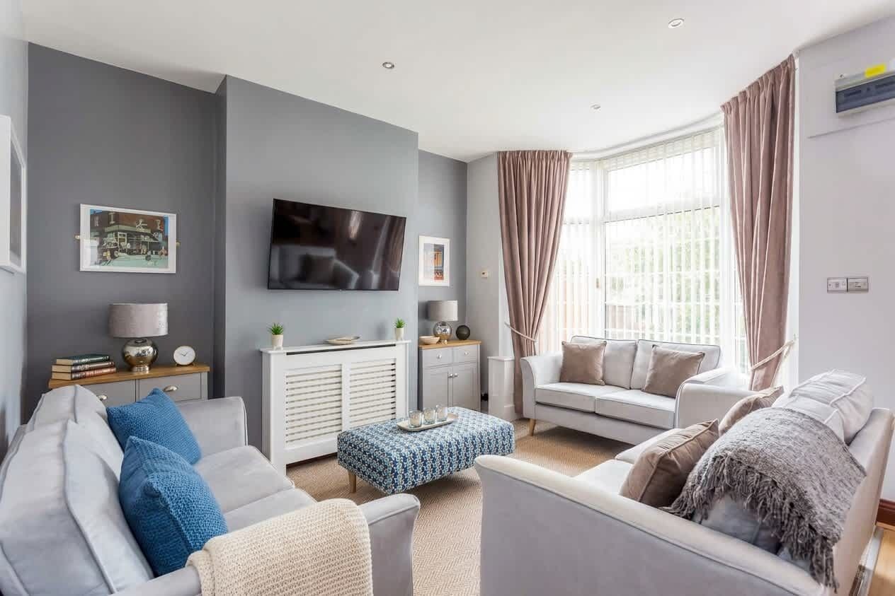 A modern living room with a grey sofa, a blue ottoman, and a television mounted on the wall.