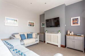 A modern living room with a grey sofa, a white cabinet, and a flat-screen TV mounted on the wall.