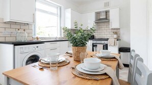 A modern kitchen with white cabinetry, a built-in washing machine, a dining table set for four, and a potted plant. - Bright & Spacious 3BED Home w Garden in St Helens (St Helens)