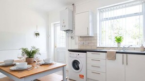 A modern kitchen with a built-in washing machine, a dining table set with plates and glasses, and a window with a view of greenery. - Bright & Spacious 3BED Home w Garden in St Helens (St Helens)