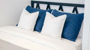 A bed with a white mattress, a blue quilted pillow, and a white pillow.