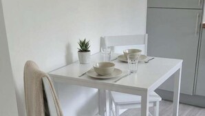 A white dining table with chairs, a small potted plant, and a glass of water.