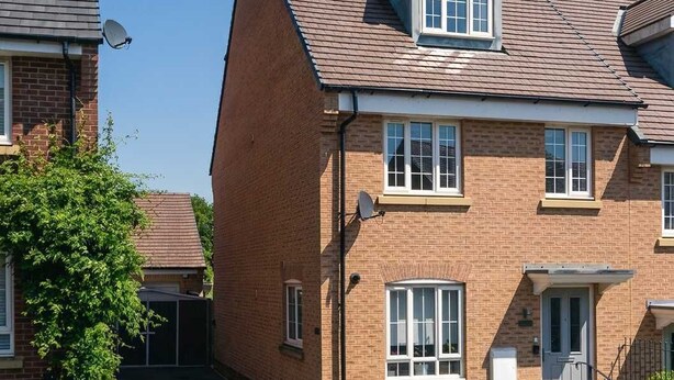 A two-story brick house with a sloped roof, a front door, and a satellite dish.