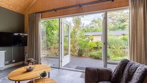 A modern living room with a wooden ceiling, a flat-screen TV, a sofa, a coffee table, and a sliding glass door leading to a garden. - Wonderful private villa for 4 guests with pool, WIFI, A/C, TV, terrace and pets allowed (Apeldoorn)