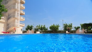 A swimming pool with clear blue water, surrounded by a building with balconies and a red lifebuoy. - Mar Internum: Family Apartment in La Pineda (La Pineda)