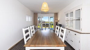 A dining area with a wooden table and white chairs, a hanging light fixture, and a view through a glass door. - Ground floor flat on the beachfront in Cambrils - 249 UHC DMS V (Cambrils)