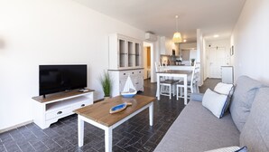 A modern living room with a flat-screen TV, a wooden coffee table, a grey sofa, and a dining area with a white table and chairs. - Ground floor flat on the beachfront in Cambrils - 249 UHC DMS V (Cambrils)