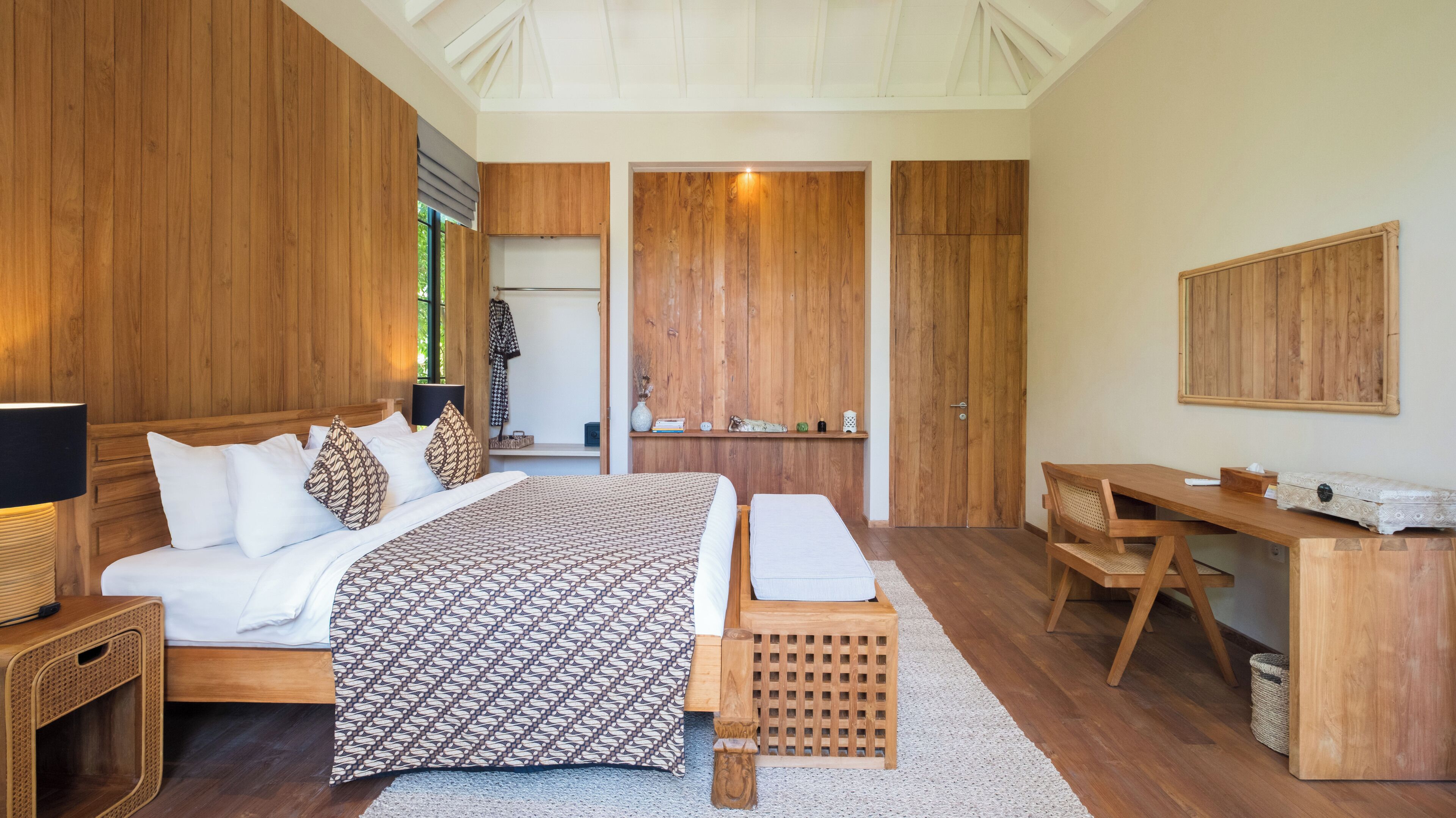 A bedroom with a large bed, a wooden desk, and a wardrobe.