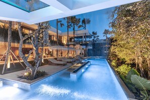 Een modern binnenzwembad met loungebedden, parasols en een waterval.