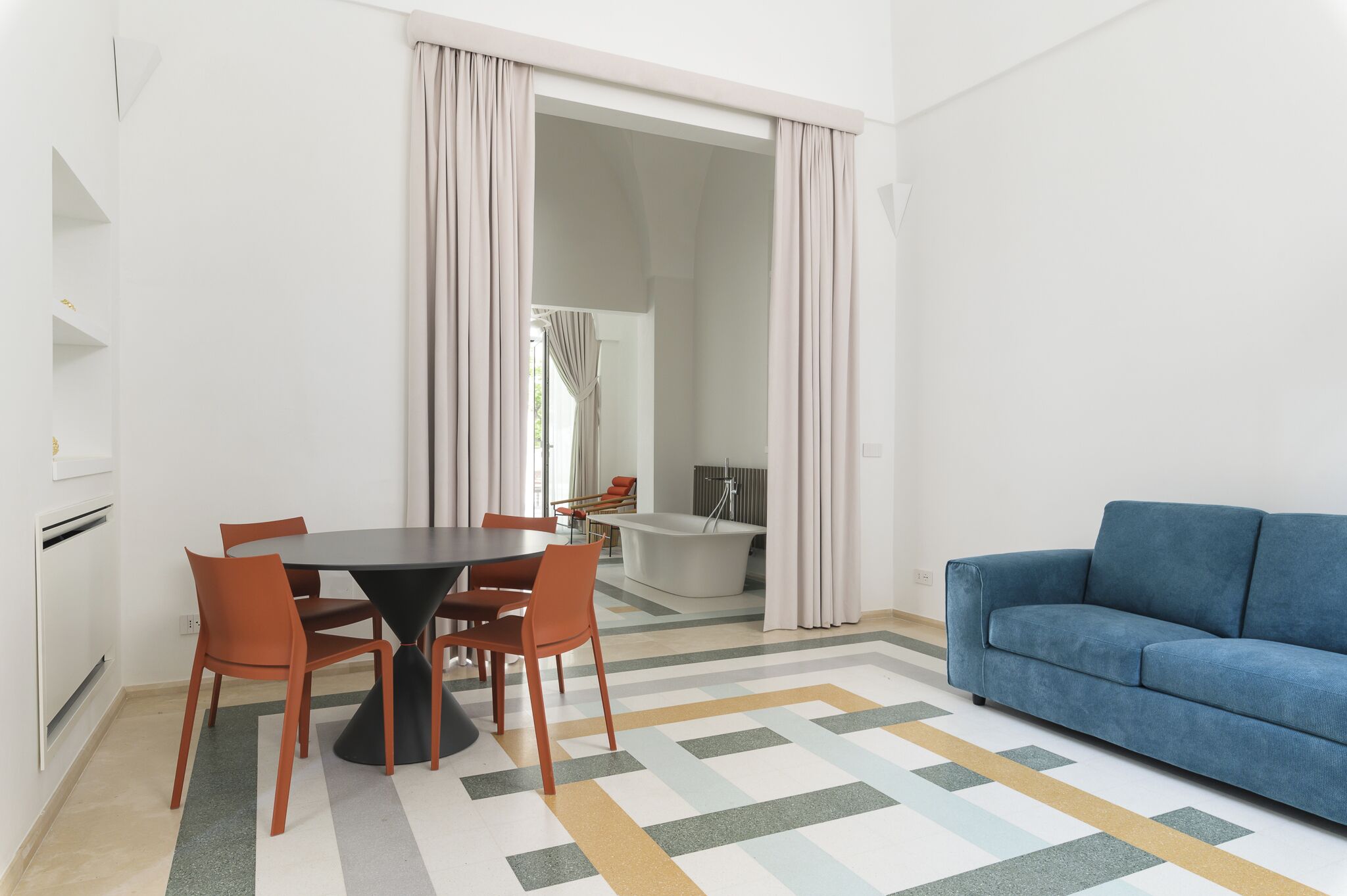 Un salon moderne avec un canapé bleu, une table à manger avec quatre chaises et une grande fenêtre avec des rideaux.