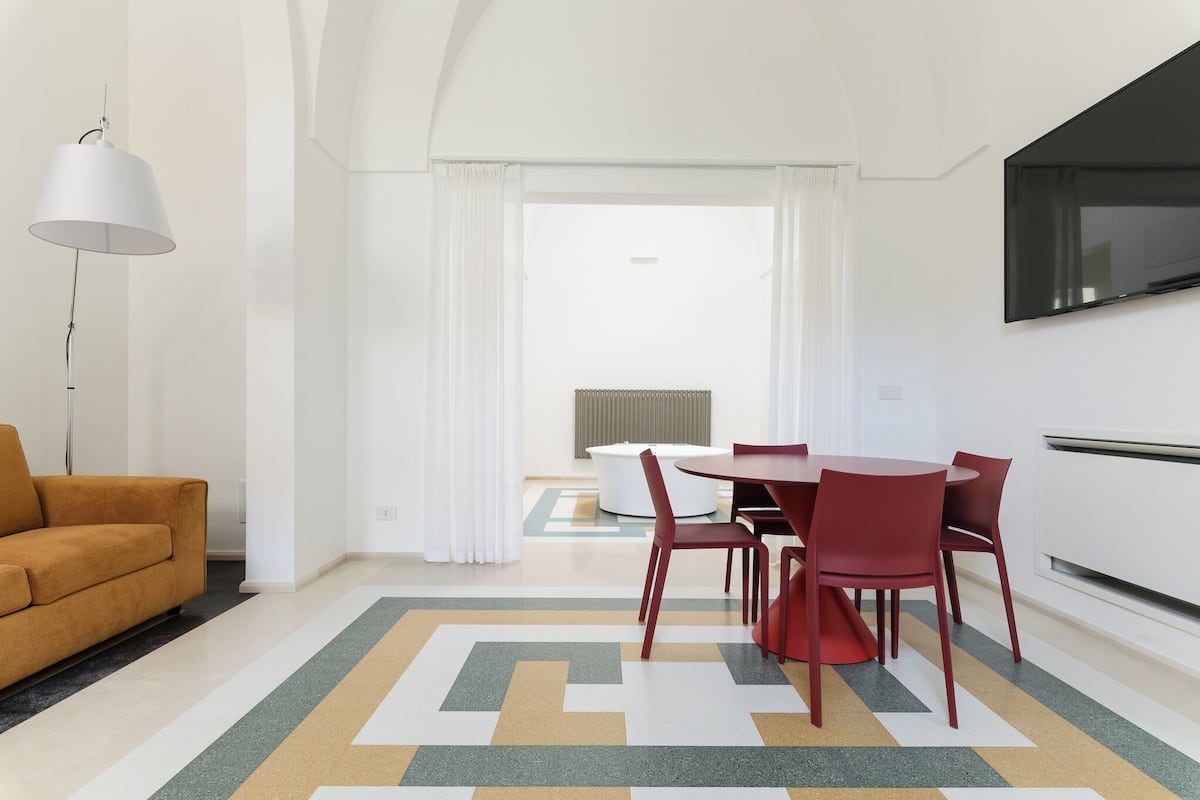 Ein modernes Wohnzimmer mit einer Couch, einem Esstisch mit Stühlen, einem an der Wand befestigten Fernseher und einem gemusterten Teppich.
