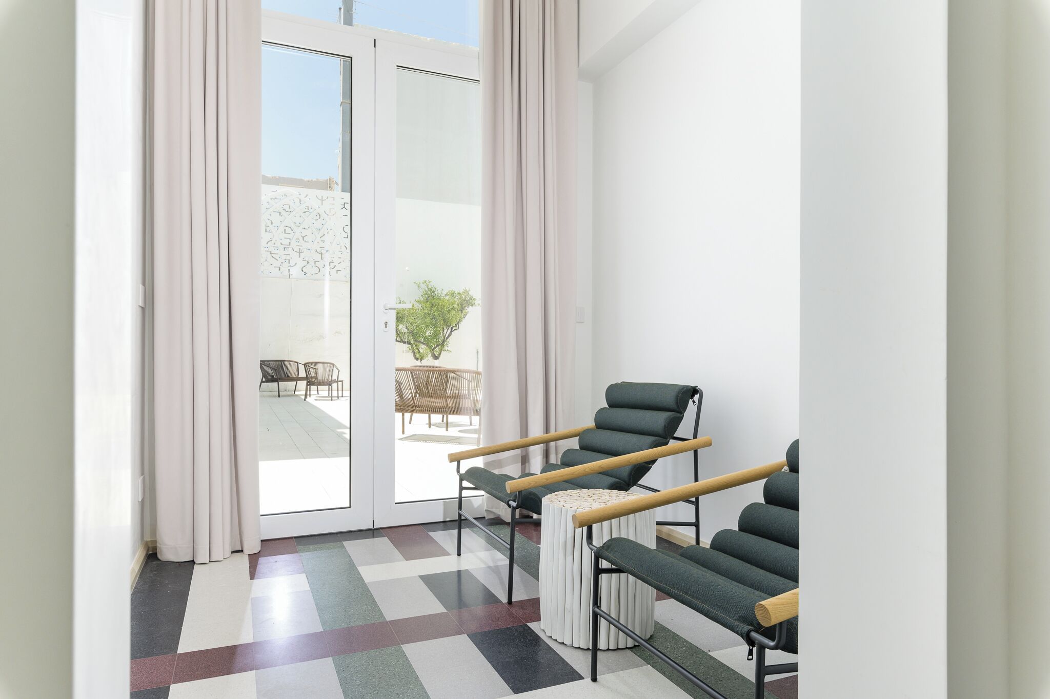A modern room with a checkered floor, a sliding glass door leading to an outdoor seating area, and a green chair with wooden armrests.