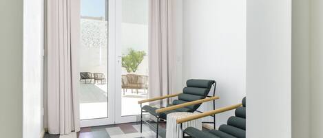A modern room with a checkered floor, a sliding glass door leading to an outdoor seating area, and a green chair with wooden armrests.