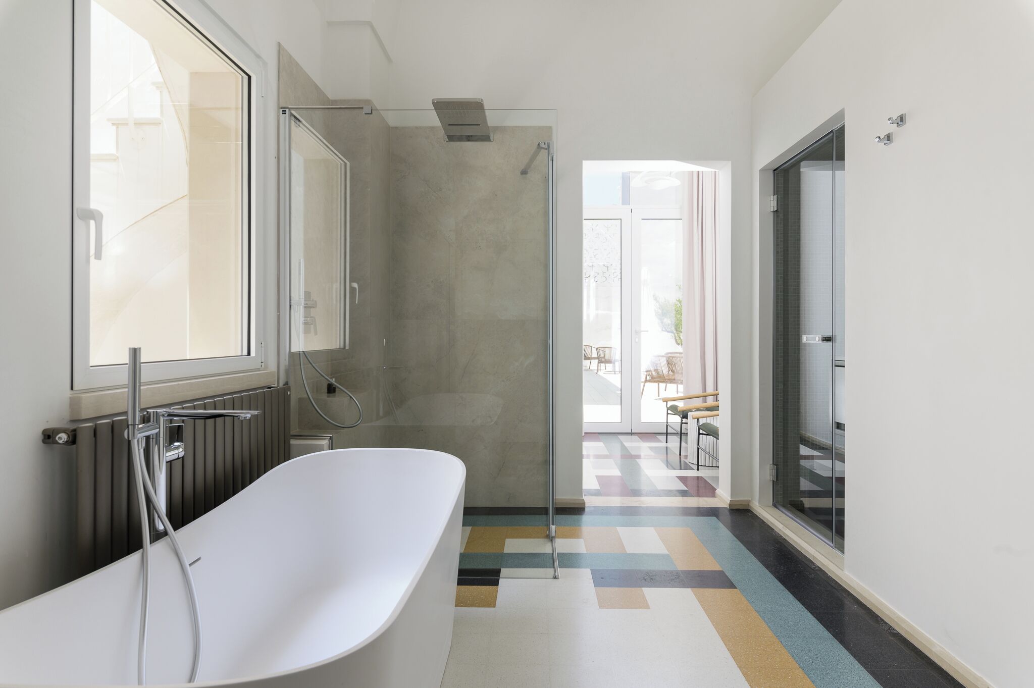 Une salle de bain moderne avec une baignoire sur pieds, une douche à parois de verre et une vue sur un balcon aménagé avec du mobilier d’extérieur.