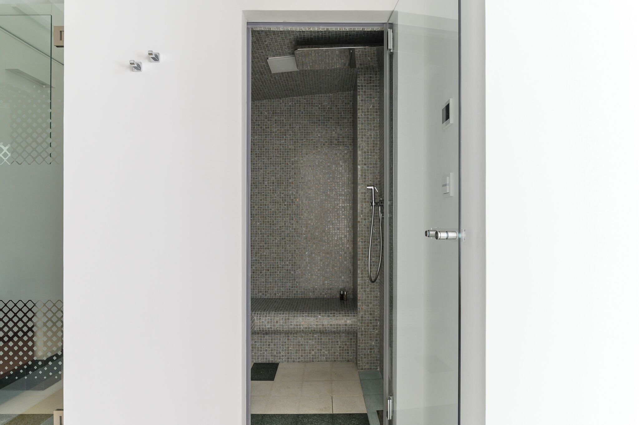 Een moderne badkamer met een glazen douchecabine, betegelde wanden en een zitbankje.