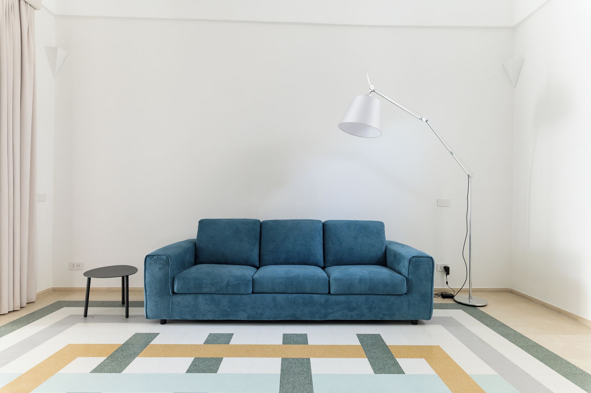 A room with a blue sofa, a small table, a floor lamp, and a patterned rug.