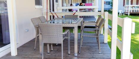 A covered outdoor patio with wicker furniture and a glass table.
