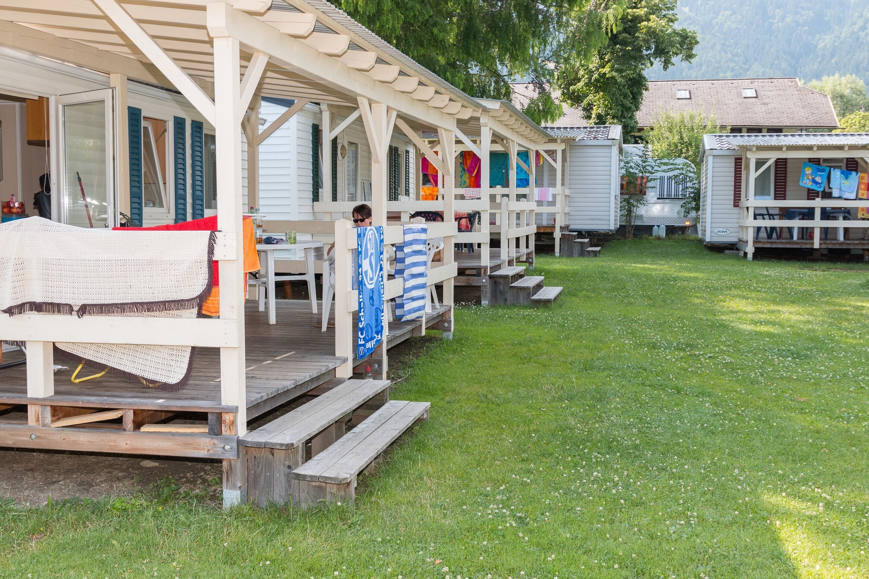 A row of mobile homes with outdoor seating areas and a grassy yard.