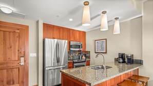Una cocina moderna con encimeras de granito, electrodomésticos de acero inoxidable, armarios de madera y una zona de bar con taburetes.