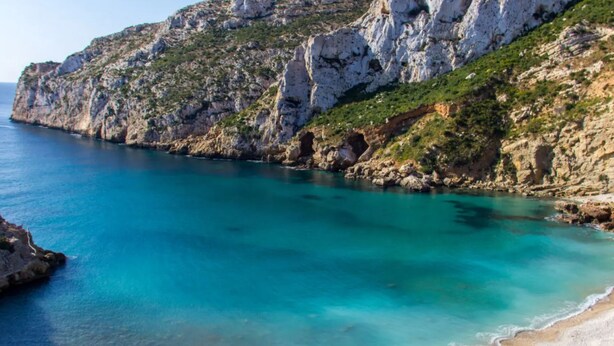 A coastal beach with clear turquoise waters, rocky cliffs, and a sandy shore. - VILLA EOS luxury villa in a quiet location (Xàbia)