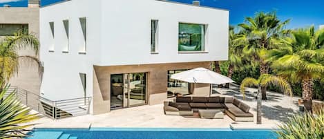 Uma casa moderna com dois andares, piscina, área de estar externa e palmeiras.