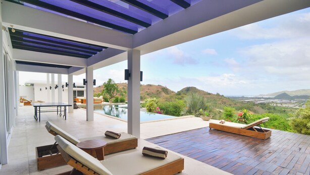 A modern outdoor lounge area with wooden loungers and a pool, overlooking a scenic landscape. - VILLA SEGER LOMBOK (Kuta)