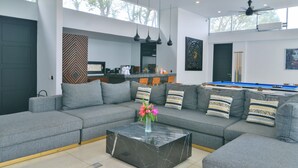 A modern living room with a grey sectional sofa, a marble coffee table, and a pool table in the background. - VILLA SEGER LOMBOK (Kuta)