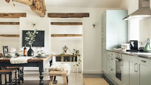 A modern kitchen with wooden beams, a dining area with a table set for four, and a view into the living area. - Jackson's Barn | Ridgestone (Water Yeat)