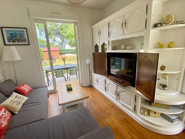 A living room with a sofa, a coffee table, a TV, and a balcony with a table and chairs.