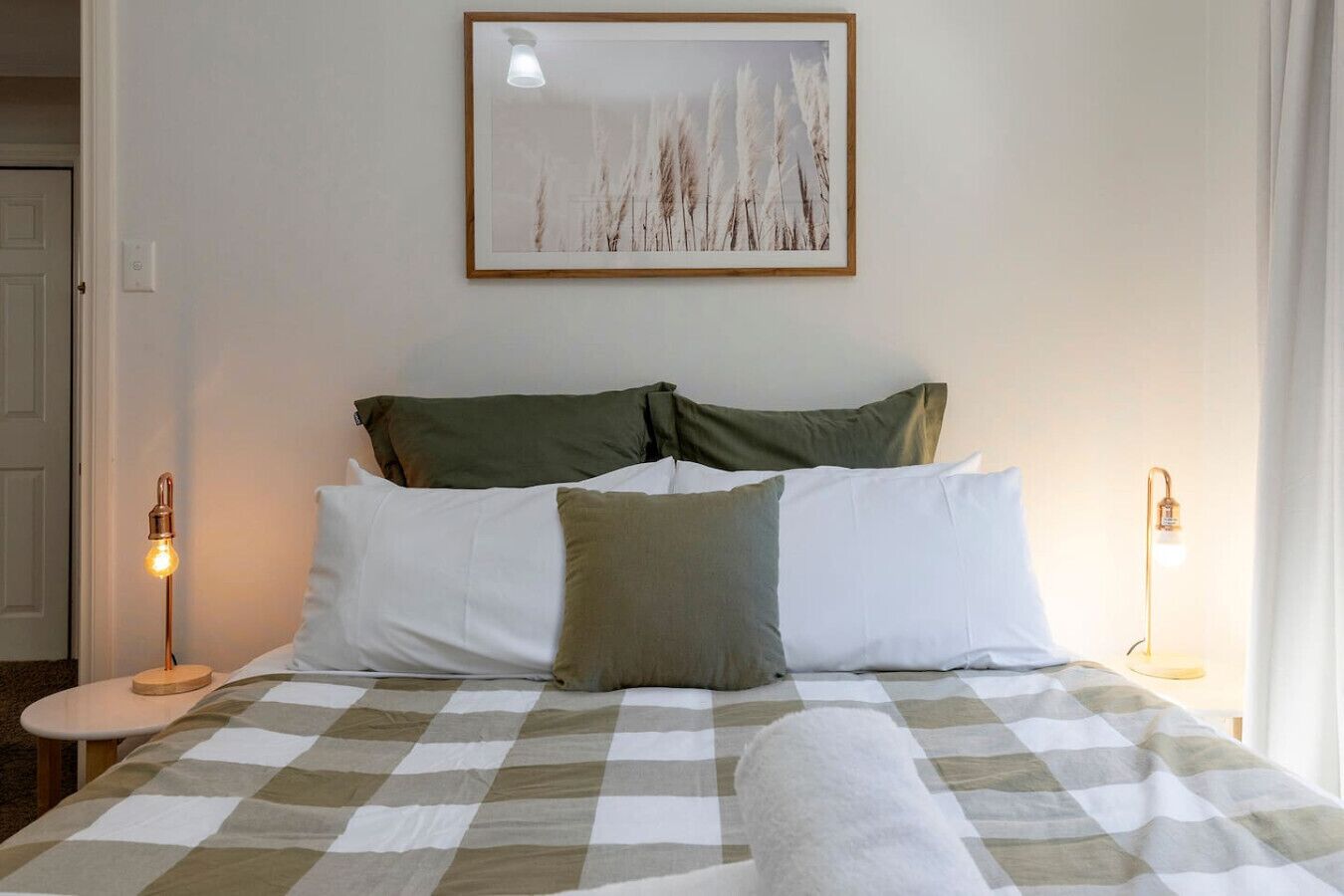 A neatly made bed with a checkered bedspread, two pillows, and two bedside lamps.